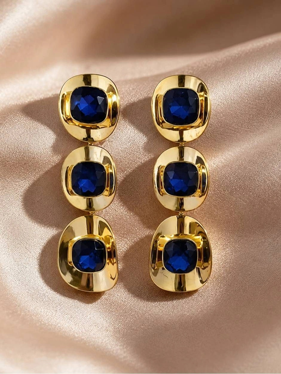 Both gold-plated blue crystal triple-drop earrings side by side on rose satin, top-down view