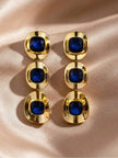 Both gold-plated blue crystal triple-drop earrings side by side on rose satin, top-down view