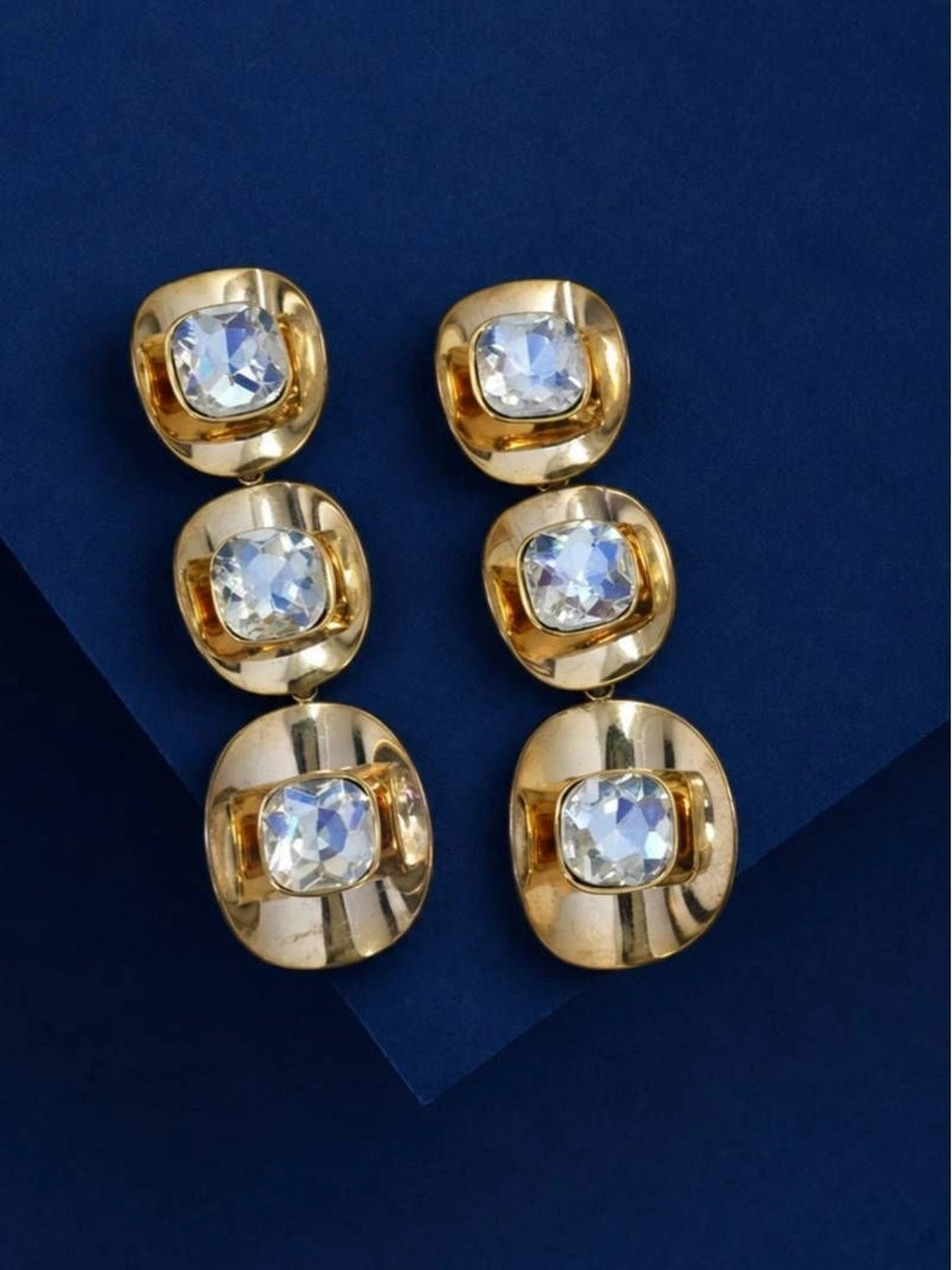 Pair of gold-plated cushion-cut crystal drop earrings laid flat on a navy blue surface