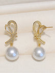 Pair of gold-plated bow earrings with pavé CZ and round pearl drops displayed on cream fabric, front view