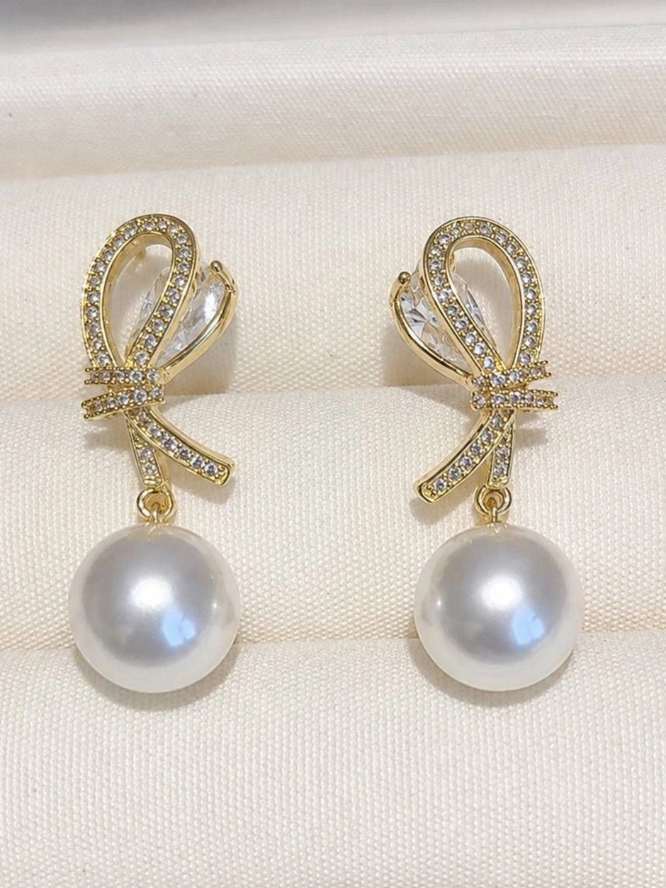 Two gold CZ bow pearl drop earrings laid flat on white fabric showing marquise crystal detail