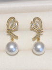 Two gold CZ bow pearl drop earrings laid flat on white fabric showing marquise crystal detail