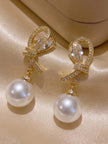 Gold bow pearl drop earrings on satin surface showing stud post and full earring length