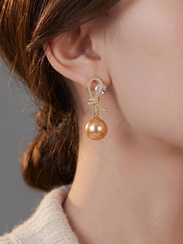 Gold-plated CZ bow and champagne shell pearl drop earring worn on a woman's ear