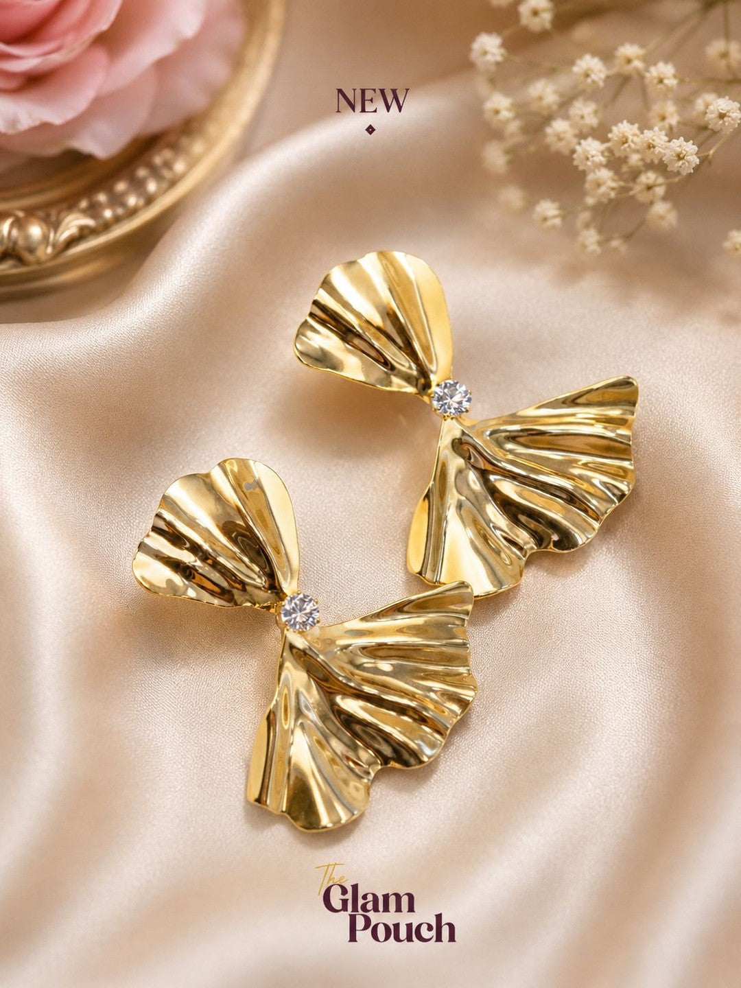 Pair of gold-plated ridged bow earrings with crystal centre on champagne satin fabric