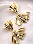 Close-up of two gold bow earrings showing high-polish ridged texture on marble surface