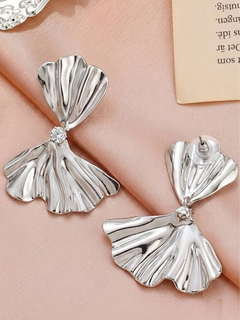Silver bow drop earrings laid flat on pink fabric, one showing front and one showing push-back stud reverse