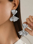 Model wearing silver bow drop earring on left ear while holding second earring near face