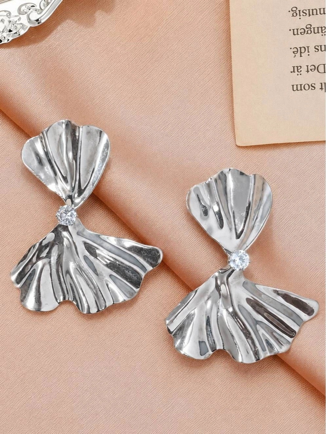 Pair of silver bow drop earrings side by side on pink fabric showing ridged fan-shaped panels
