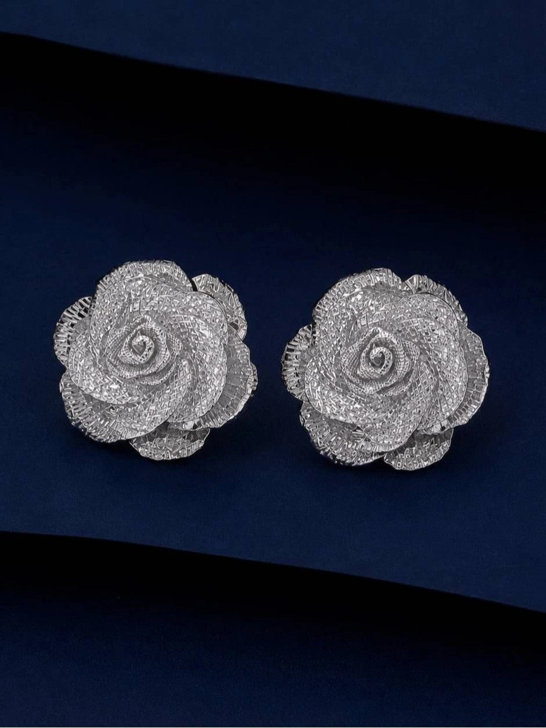 Pair of silver-finish rose stud earrings with textured mesh petals on a navy background