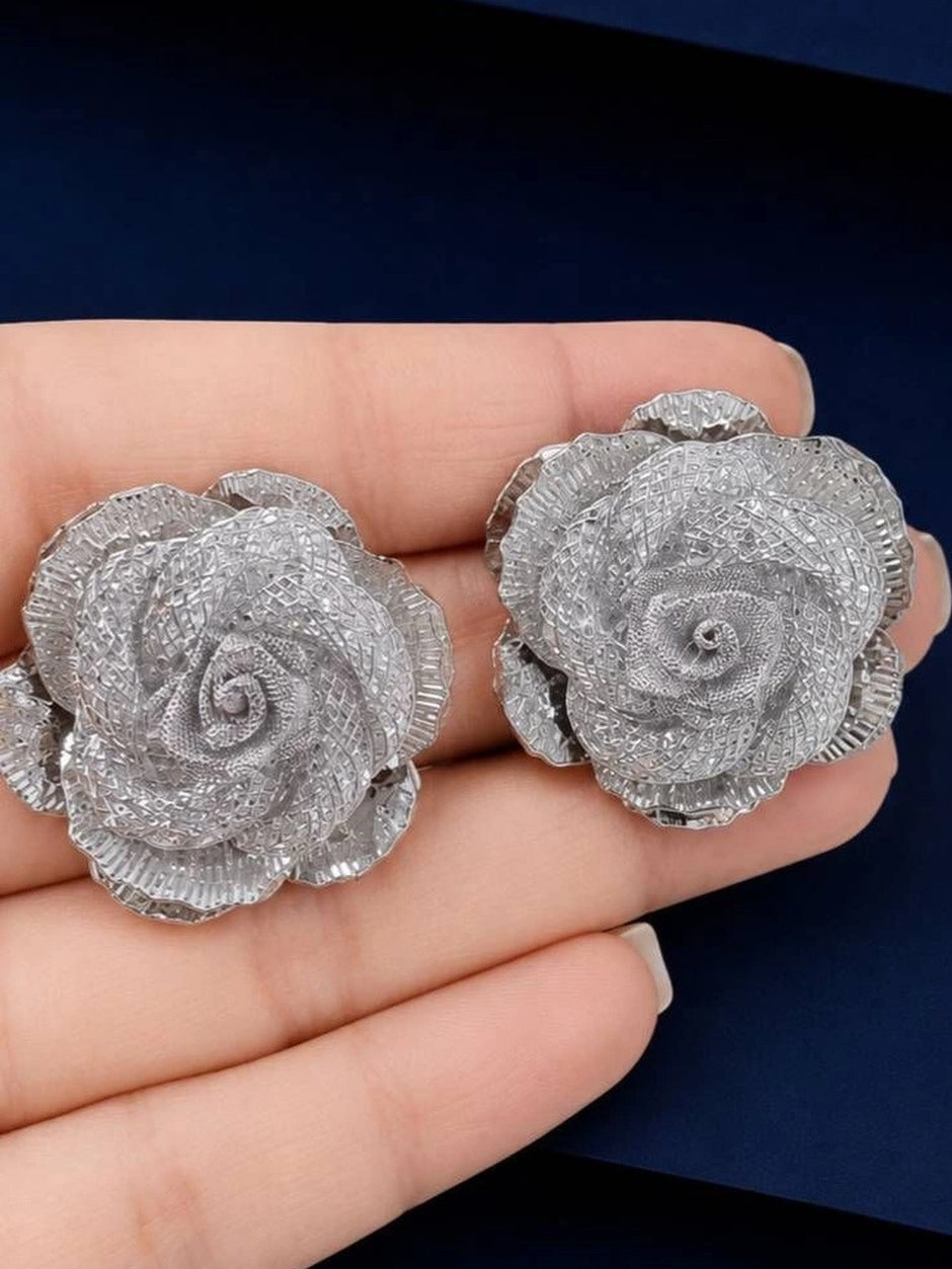 Close-up of two silver rose stud earrings resting on an open palm showing petal detail