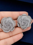 Close-up of two silver rose stud earrings resting on an open palm showing petal detail