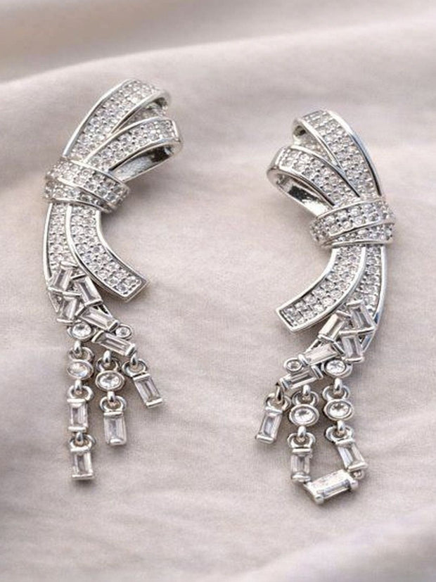 Pair of silver-toned CZ bow drop earrings laid flat on a cream fabric background