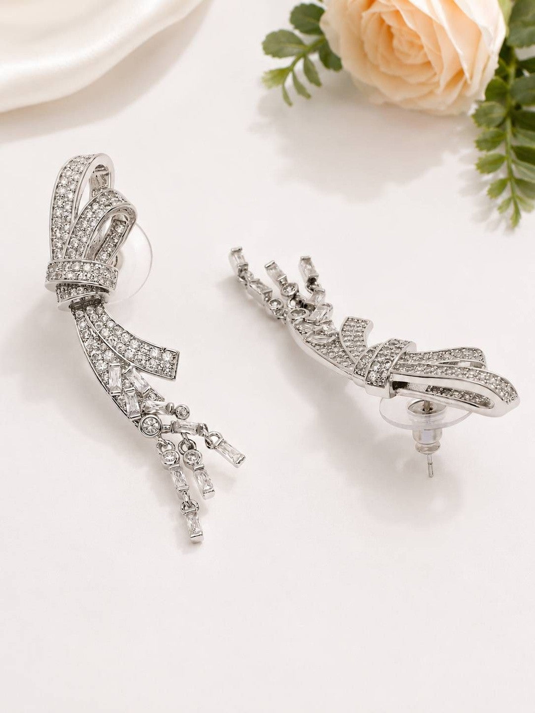 Side and back view of CZ bow earrings showing push-back post and rubber stopper near a peach rose