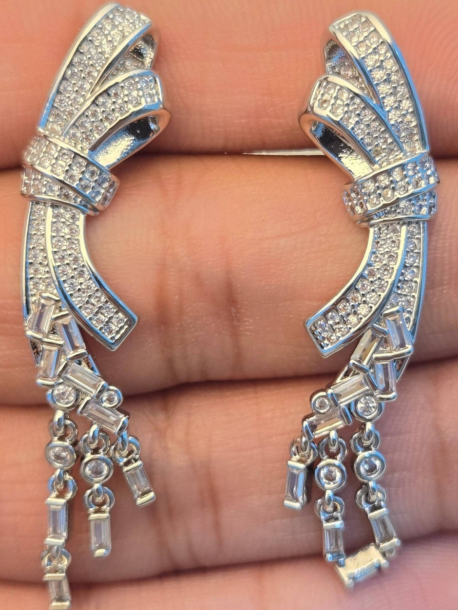 Close-up of both silver CZ bow drop earrings held in an open palm showing pavé detail