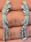 Close-up of both silver CZ bow drop earrings held in an open palm showing pavé detail