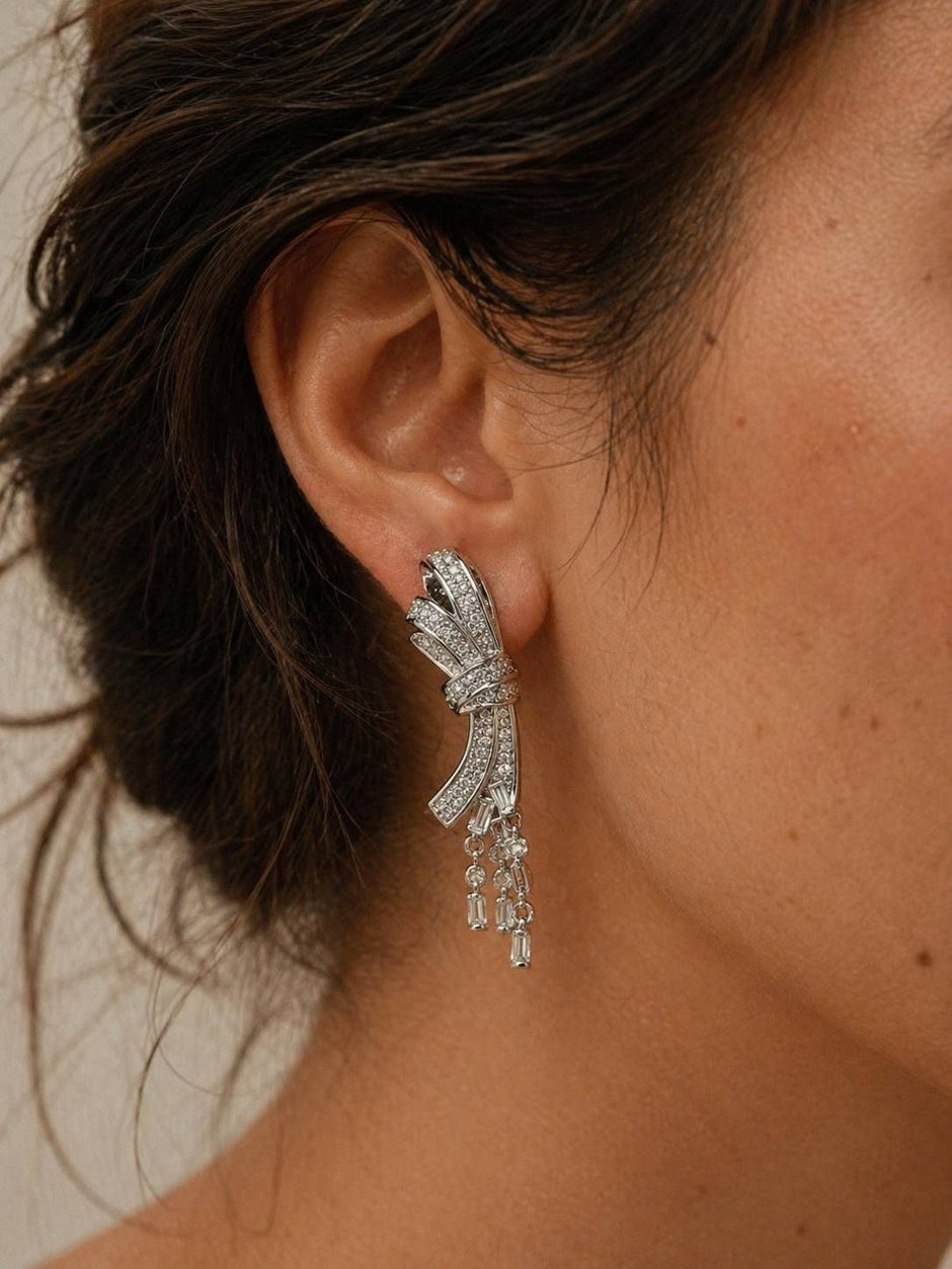 Silver CZ bow drop earring worn on a woman's ear showing full length and drape