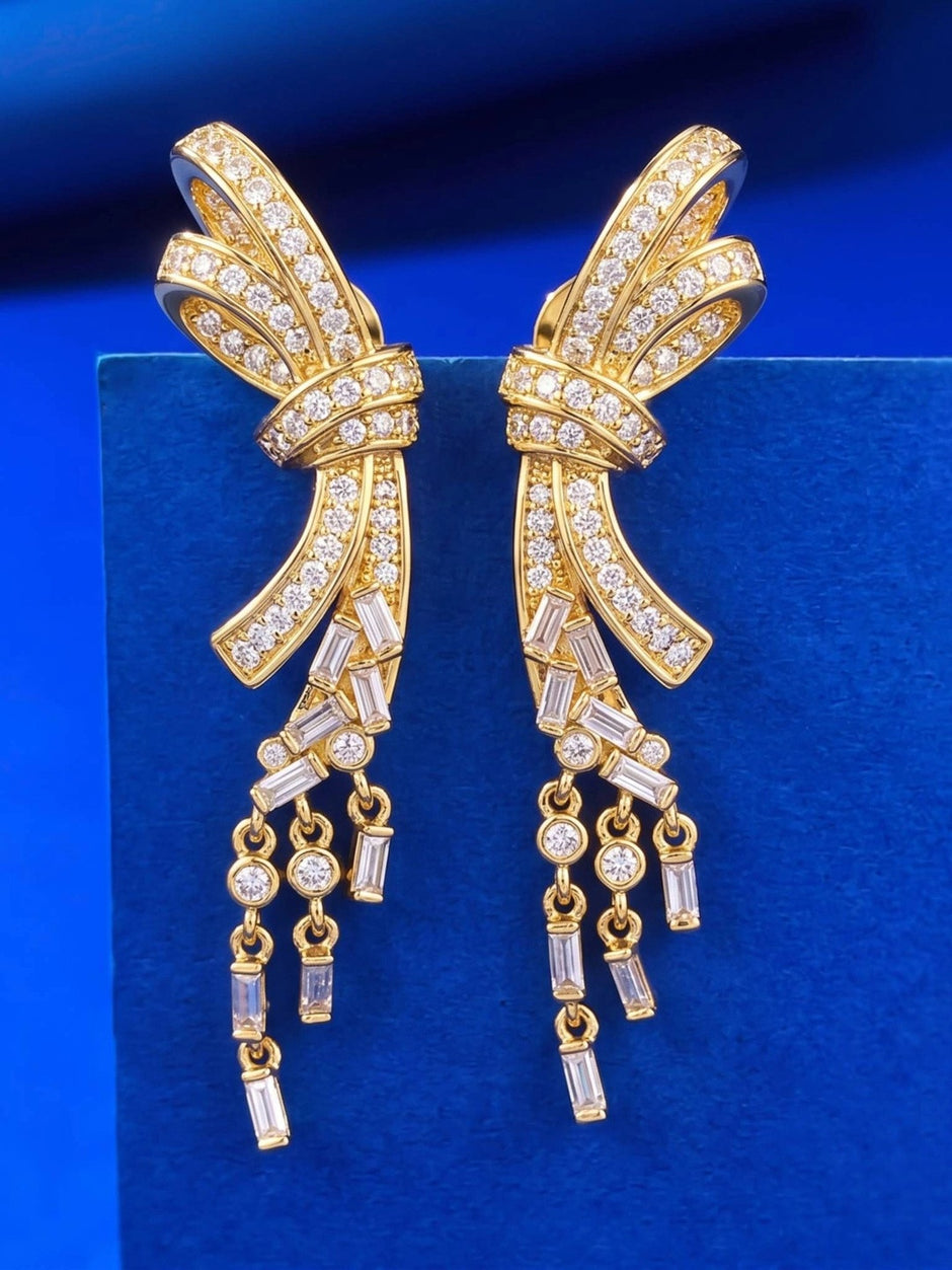 Pair of gold-plated bow drop earrings with CZ pavé and baguette tassel dangles on a blue velvet display tray
