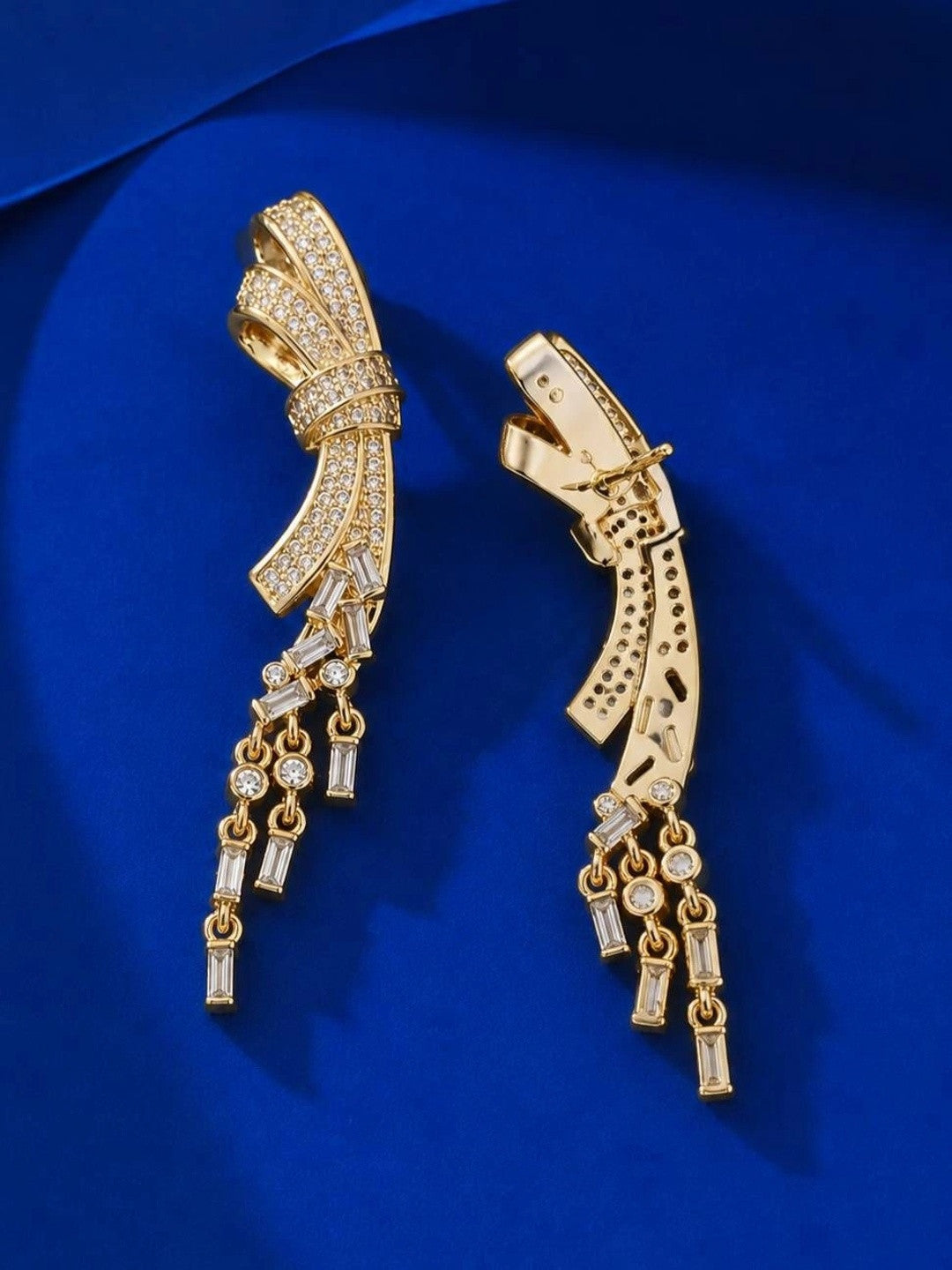 Side and back view of gold bow drop earrings showing clip fitting and CZ tassel drops on blue satin