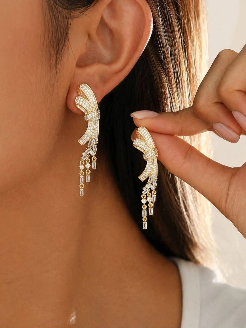 Model wearing gold bow CZ drop earrings on ear showing full length and movement of tassel dangles