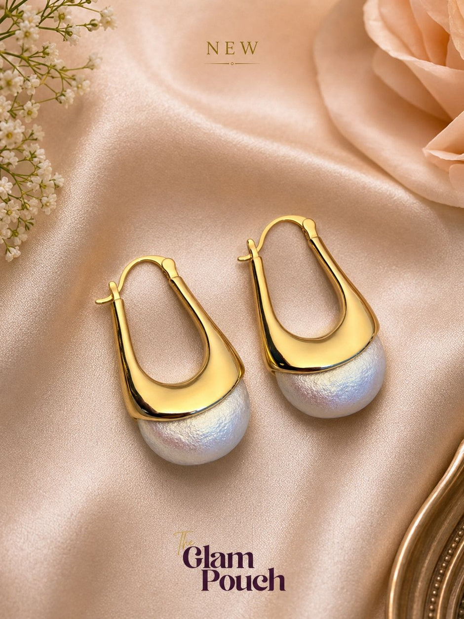 Pair of gold vermeil elongated hoop earrings with ivory pearl drops on peach satin fabric