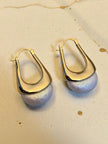 Close-up of gold hoop pearl drop earrings laid flat on a pale textured surface