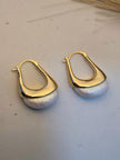 Pair of gold and pearl hoop earrings side by side on a white surface near dried grass