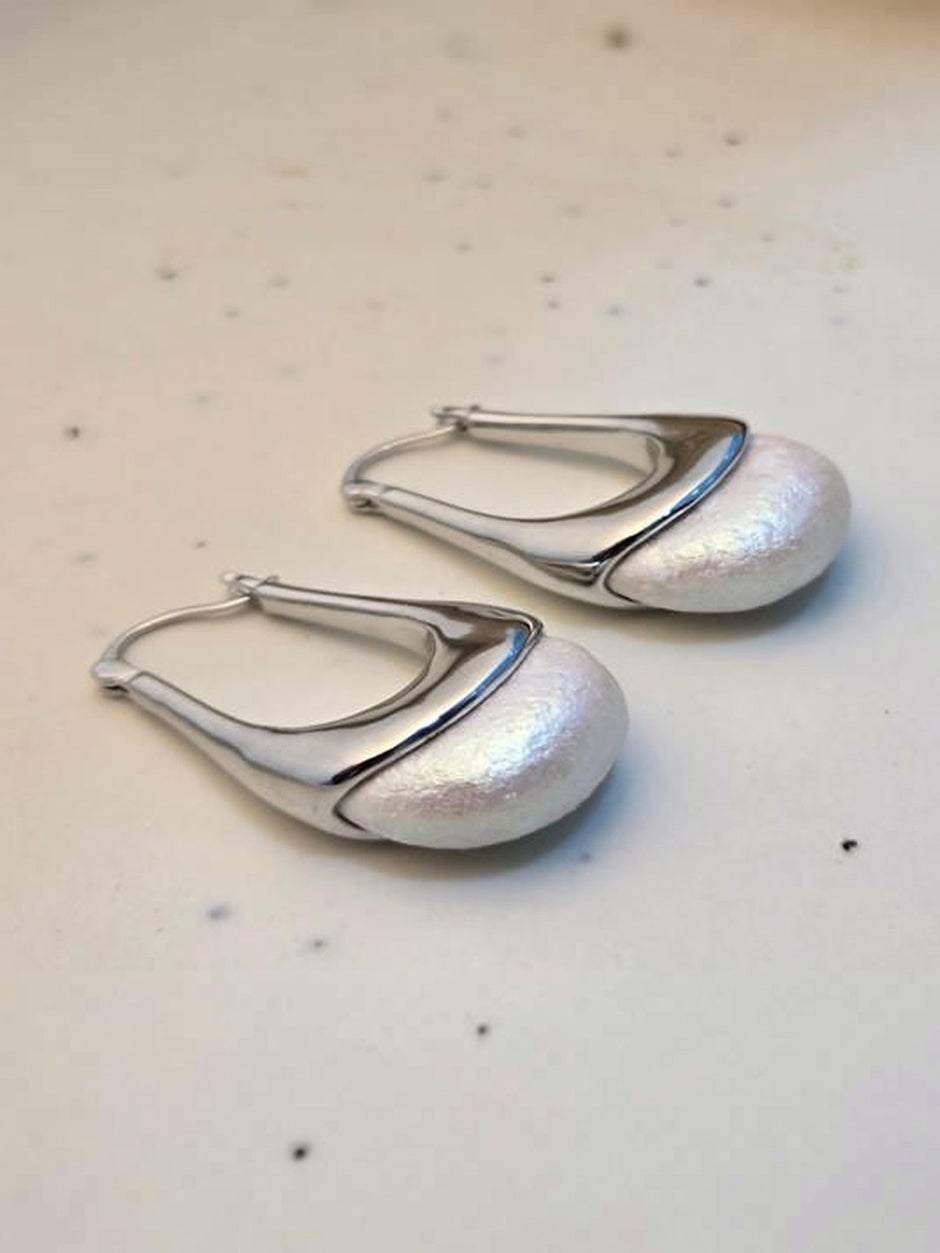 Pair of silver-finish pearl dome hoop earrings laid flat on a light speckled surface, showing lever-back closure