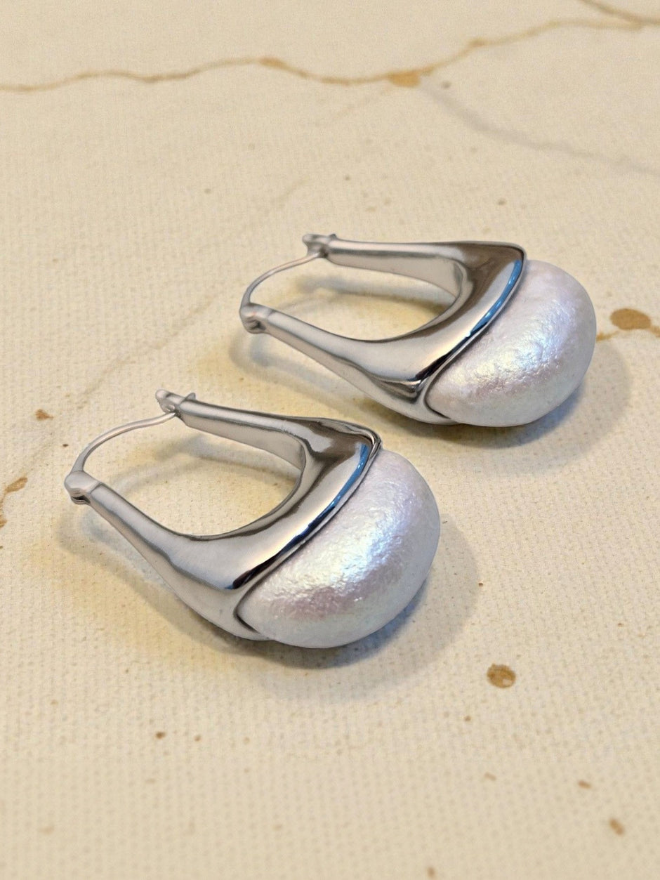 Two silver hoop earrings with iridescent pearl dome base resting on a textured cream fabric background