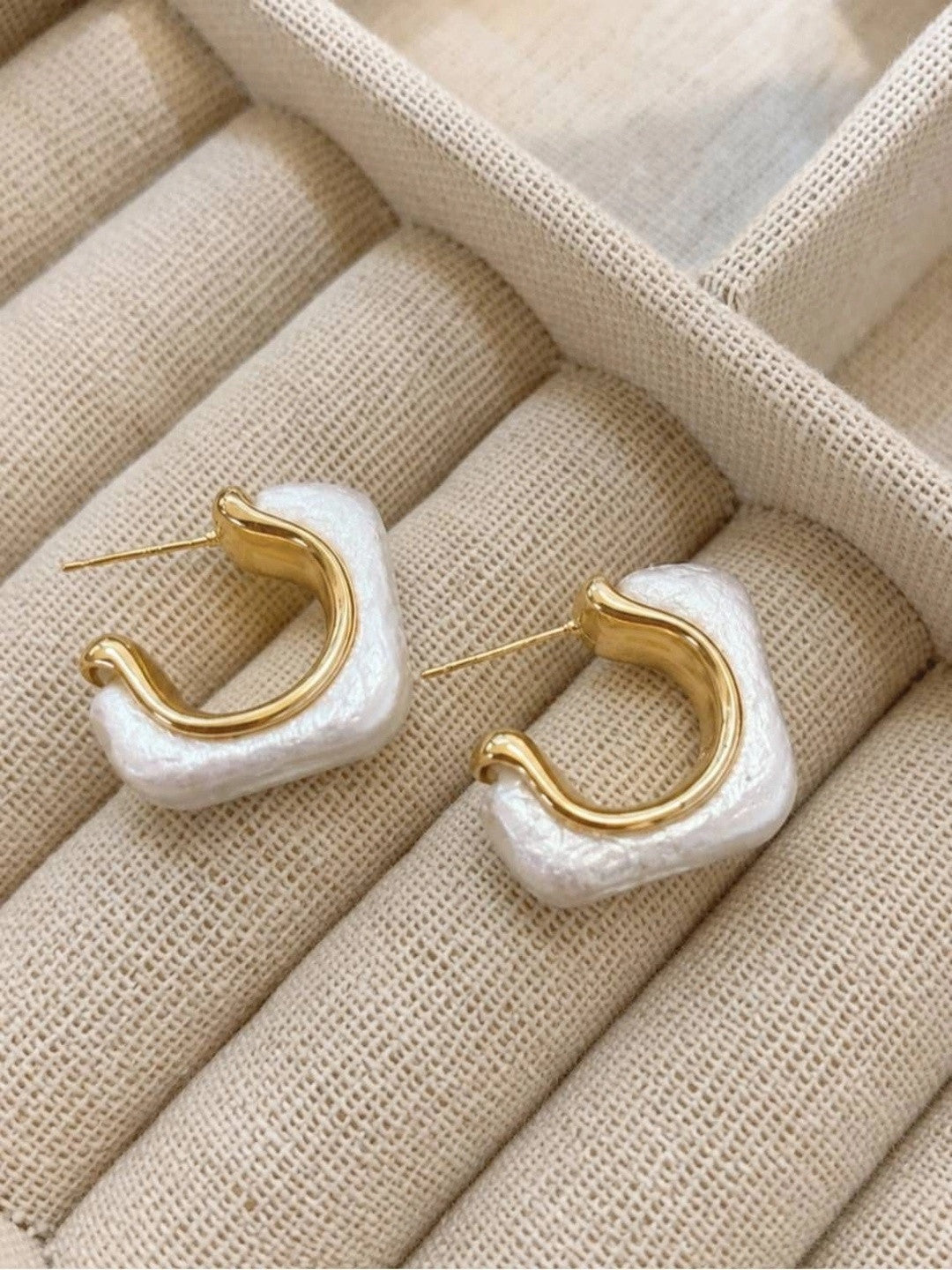 Pair of gold-plated pearl resin geometric hoop earrings laid flat on a cream jewellery tray