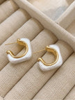 Pair of gold-plated pearl resin geometric hoop earrings laid flat on a cream jewellery tray