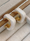 Two pearl resin geometric hoop earrings standing upright against wooden jewellery box edge
