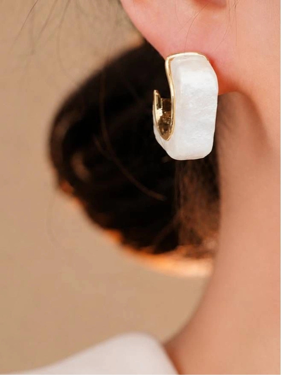 Pearl resin geometric hoop earring worn on a model's ear with dark hair pinned up
