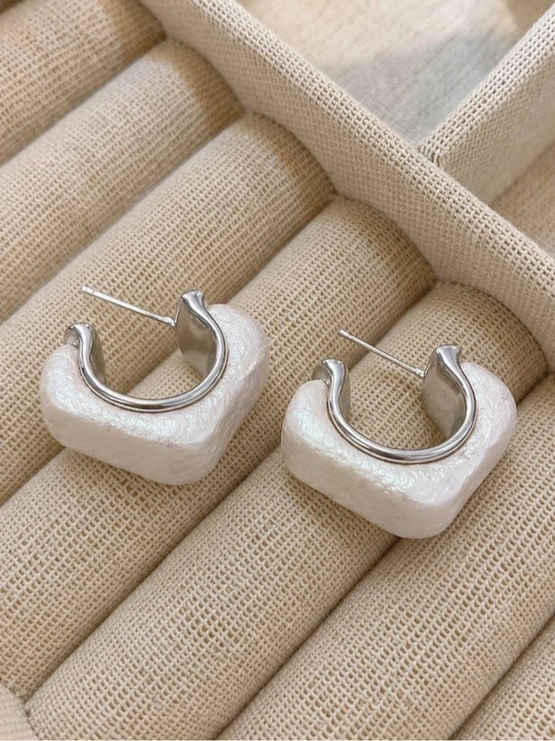 Pair of pearl-white resin geometric half hoop earrings with silver-tone metal, laid flat in a beige jewellery tray