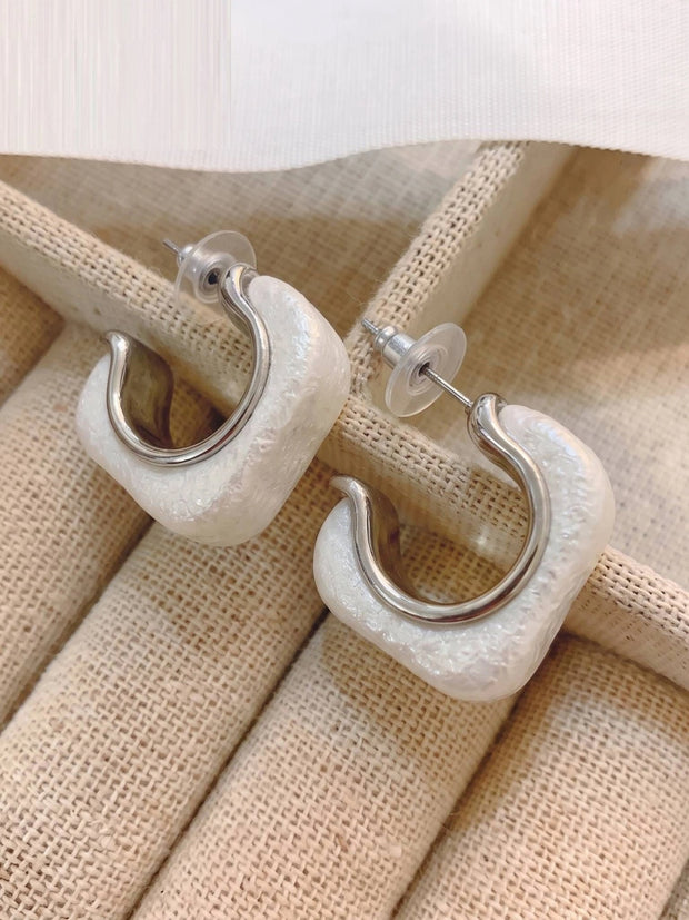 Close-up of two white resin square half hoop earrings showing rubber stopper backs on burlap surface