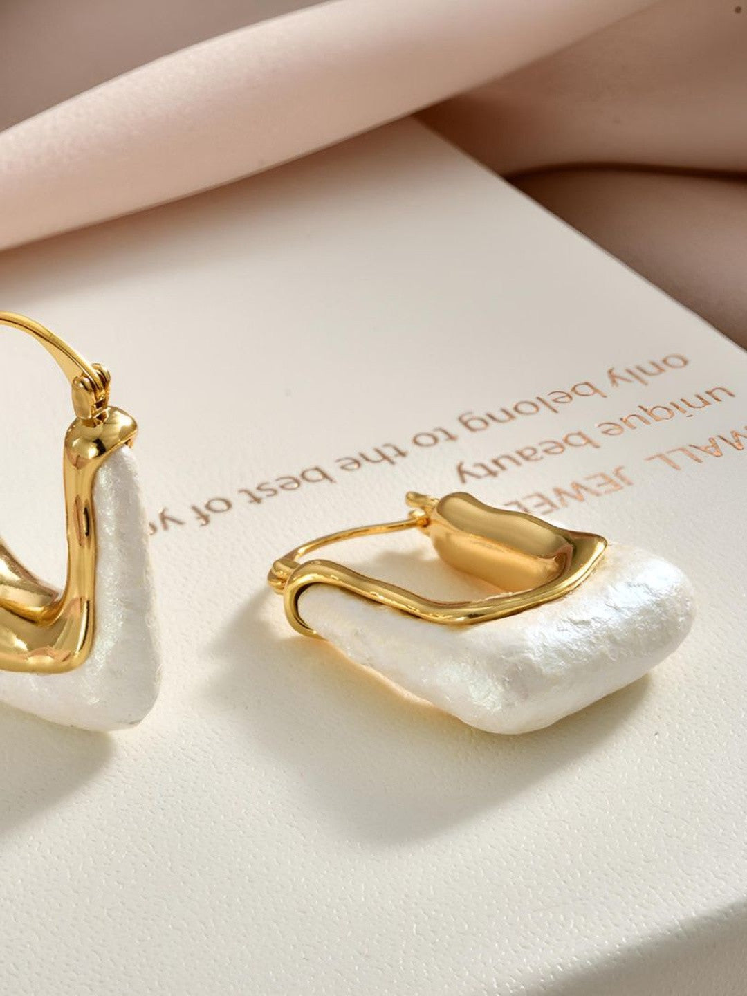 Close-up of gold-plated pearl hoop earrings resting on a branded jewellery box showing texture and click-top closure detail