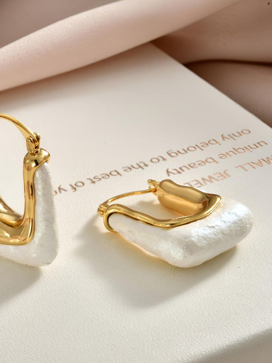 Close-up of gold-plated pearl hoop earrings resting on a branded jewellery box showing texture and click-top closure detail