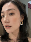 Woman wearing one gold-plated baroque pearl hoop earring, shown from a side angle against a warm indoor background