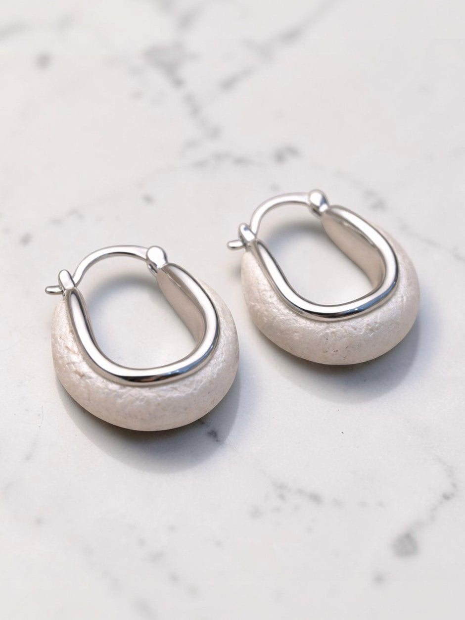 Two silver-tone oval hoop earrings with chunky stone-look base displayed on white marble surface
