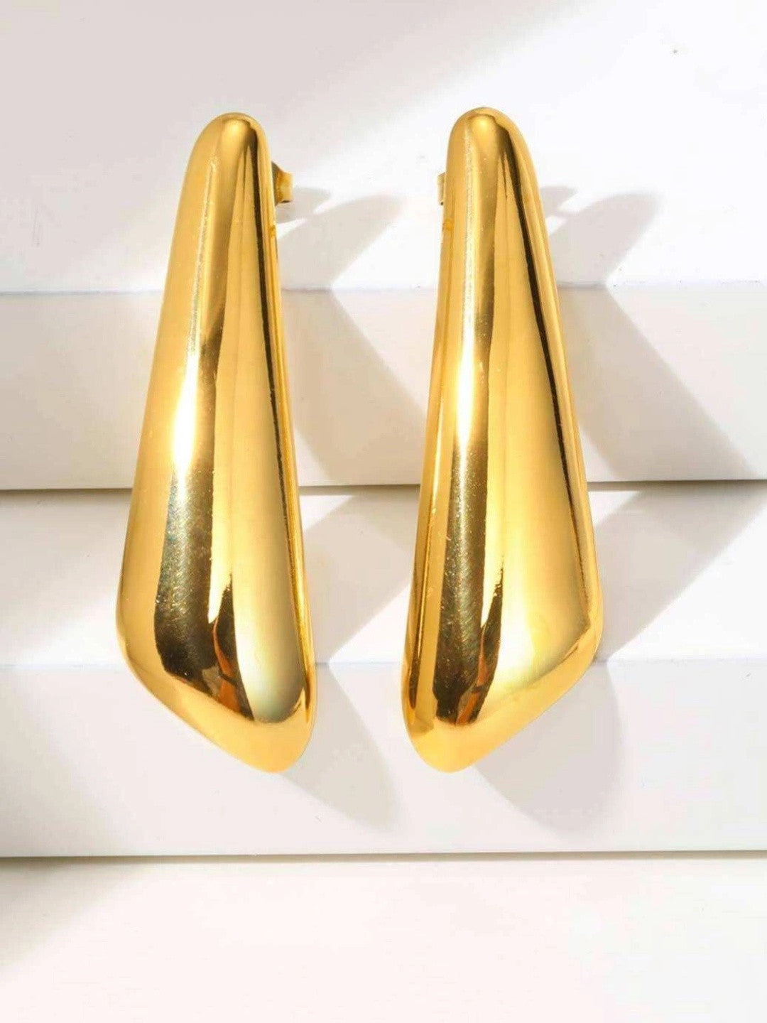 Pair of gold-toned geometric tapered drop earrings standing upright on a white surface, front view