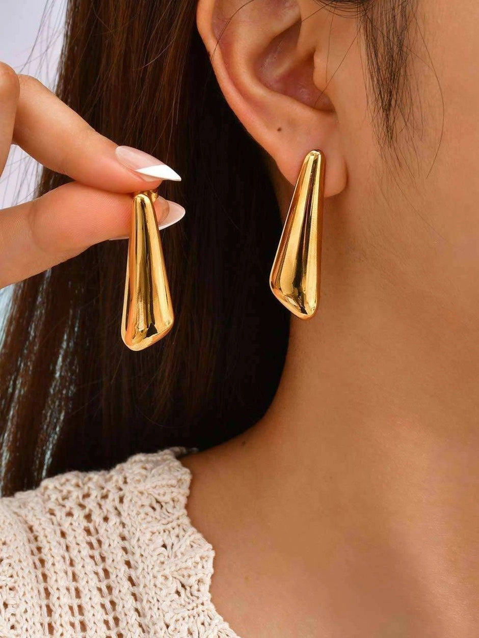 Model wearing gold-toned geometric tapered drop earrings, shown from both ears against dark hair