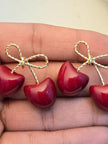 Two pairs of deep red enamel cherry bow earrings resting on an open palm showing scale and finish detail