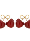 Close-up of two red enamel cherry double-drop earrings with gold-toned twisted-wire bows on a white background
