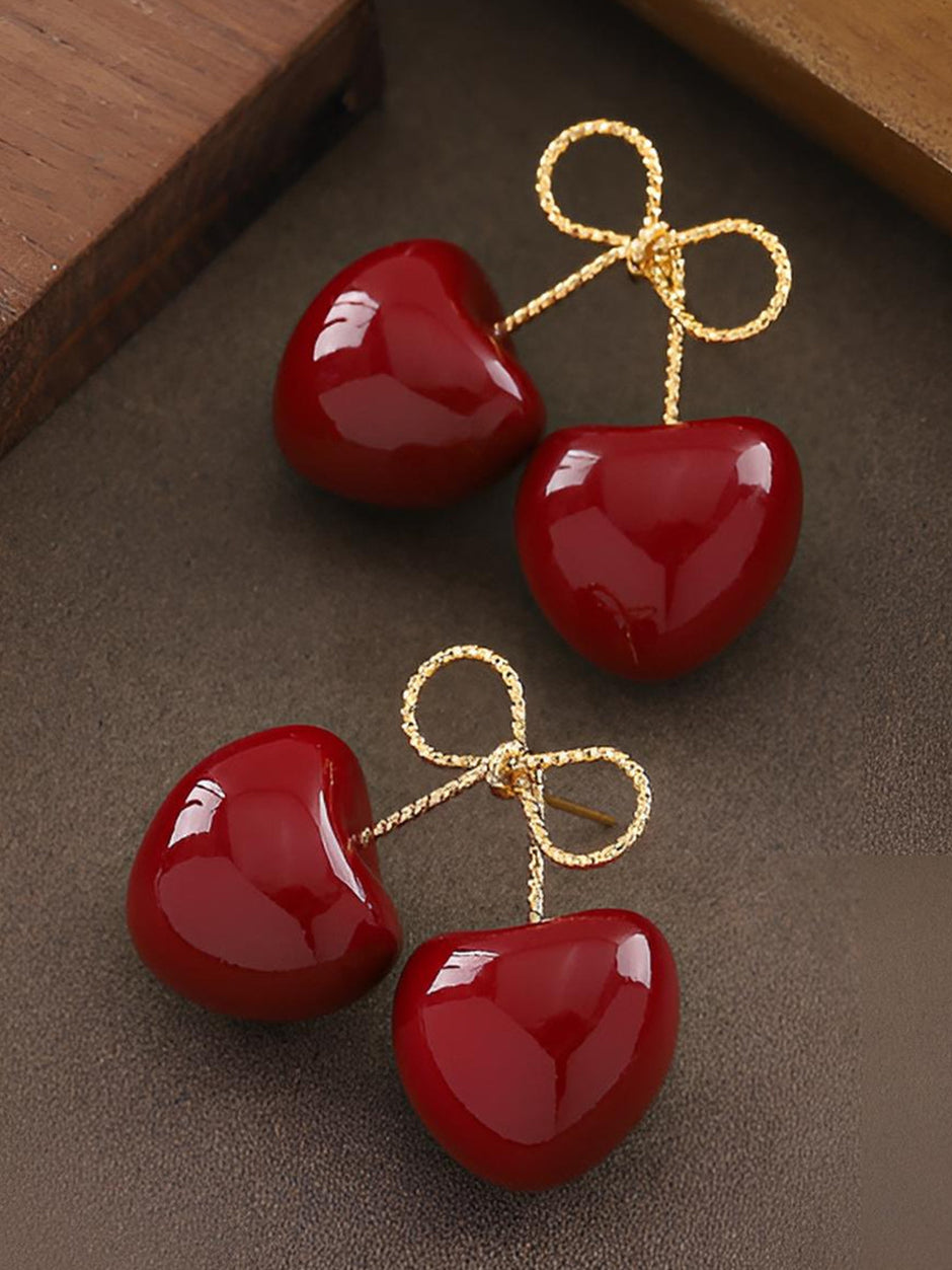 Pair of red enamel cherry earrings with gold bow tops displayed flat on a clean white background
