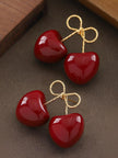 Pair of red enamel cherry earrings with gold bow tops displayed flat on a clean white background