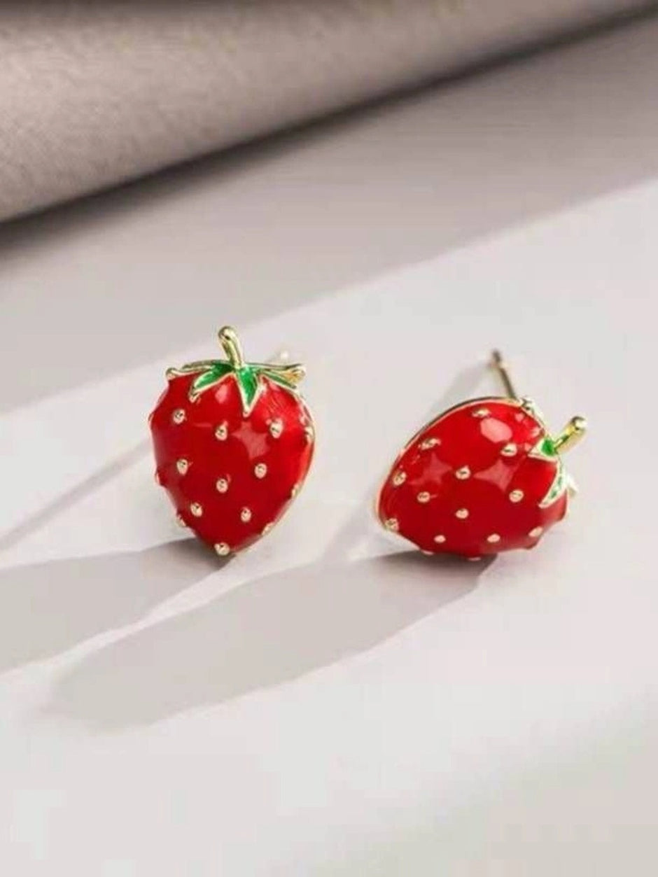 Two red enamel strawberry stud earrings with gold-toned detailing placed on a white surface in soft light
