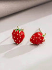 Two red enamel strawberry stud earrings with gold-toned detailing placed on a white surface in soft light