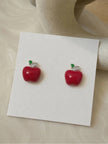 Pair of red enamel apple stud earrings displayed on a white card with silver-tone crystal leaf detail