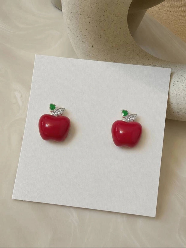 Pair of red enamel apple stud earrings displayed on a white card with silver-tone crystal leaf detail
