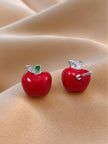 Close-up of red apple stud earrings showing push-back post and silver leaf setting on skin